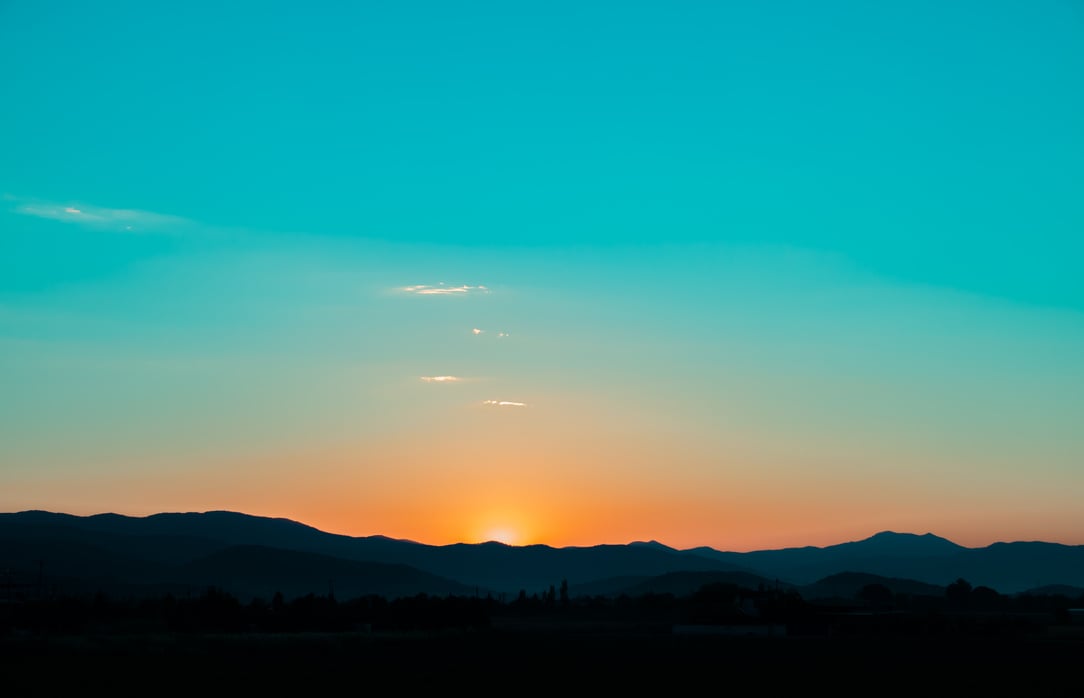 Sunrise turquoise sky and orange sun behind mountains.